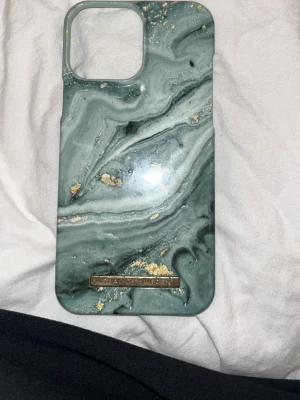 Grönt marmormönstrat mobilskal iDeal -  Till iphone 13 pro max Snyggt mobilskal från iDeal of Sweden med grönt marmormönster och guldfärgade detaljer.  Skalet har en glansig finish och en metallbricka med loggan längst ner. Passar perfekt för dig som vill ha ett unikt och trendigt skydd till mobilen.