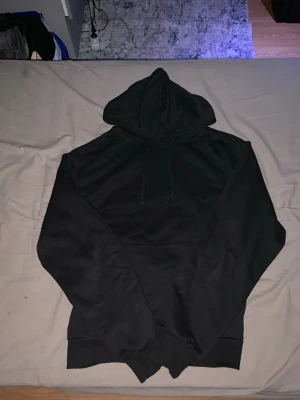 Svart hoodie från Take Off - En stilren svart hoodie från Take Off med klassisk huva och dragsnören. Hoodien har en rymlig ficka framtill och ribbade muddar vid ärmslut och nederkant. Perfekt för en avslappnad och cool look.