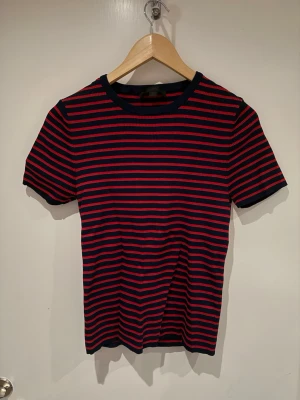 Randig t-shirt från Zara i marinblått och rött - Säljer en snygg randig t-shirt från Zara i marinblått och rött. T-shirten har korta ärmar, rund halsringning och är gjord i ett mjukt bomullsmaterial. Perfekt för en avslappnad och trendig look.