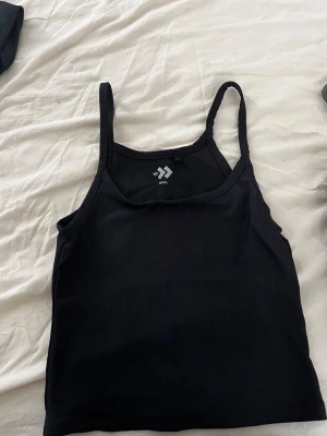 Svart och gråbrun ribbad crop top  - Svart och grå/brun  ribbad crop top med smala axelband och rundad halsringning. Perfekt för träning eller chill dagar, tillverkad i stretchigt material som sitter skönt mot kroppen.