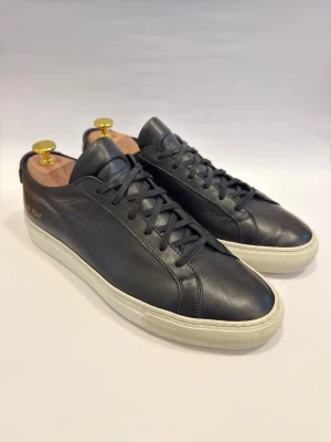  Common Projects Achilles Low 40 - Ikoniska lyxsneakers! Common Projects är för dig som tröttnat på Goose och Lanvin. Detta är orginalet när det gäller minimalism. Mycket fint skick på skorna och nära nyskic! Skoblock ingår inte. Stora i storleken så dessa passar dig med storlek 41