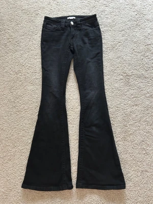 Svarta utsvängda jeans - Snygga svarta jeans med utsvängda ben och dekorativa nitar på bakfickorna. Klassisk femficksmodell med knapp och dragkedja framtill. Det är aldrig använda.