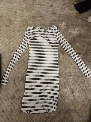 Vit och marinblå randig klänning Bik Bok - Säljer en vit ribbad klänning från Bik Bok med svarta horisontella ränder. Klänningen har lång ärm, kroppsnära passform och är i kort modell. .