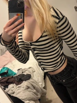 Svartvit randig croppad topp -  croppad topp med svartvita ränder och långa ärmar. Toppen har knappar framtill och en djup v-ringning som ger en snygg look. Perfekt att matcha med höga jeans eller kjol.