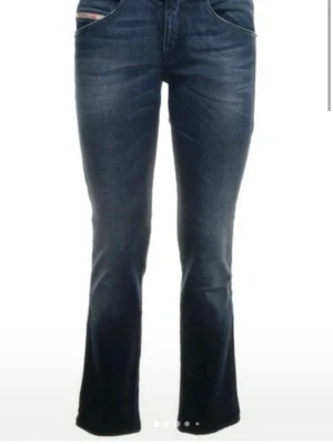 Mörkblå bootcut jeans från Diesel - Snygga mörkblå bootcut jeans från Diesel med klassisk femficksdesign och subtila slitningar framtill. Jeansen har dragkedjedetaljer på bakfickorna och är tillverkade i ett mjukt denimtyg som sitter skönt. Perfekta för en trendig och avslappnad look.