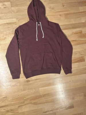 Pier one hoodie - En stilren vinröd hoodie från pier one med klassisk känguruficka och vita dragsnören i huvan. Hoodien har ribbade muddar vid ärmar och nederkant. Perfekt för en avslappnad och trendig look. Materialet känns mjukt och bekvämt, troligen bomullsblandning.