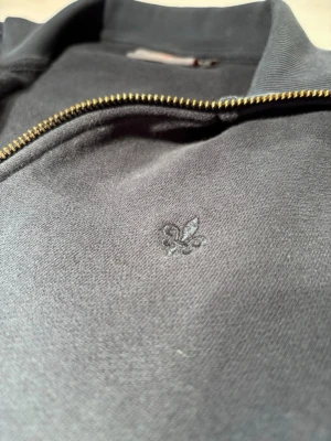 Morris zip - Snygg mörkblå Morris tröja med dragkedja och ståkrage. Tröjan har två sidofickor och en diskret broderad logga på bröstet. Tillverkad i mjukt bomullsmaterial som känns skönt mot huden. Perfekt för en avslappnad och stilren look.