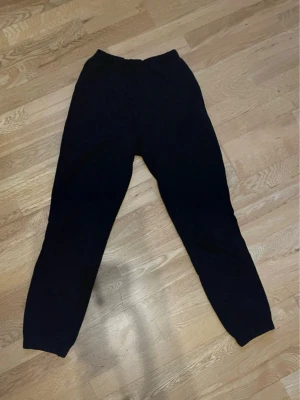 Svarta mjukisbyxor med resår - Ett par klassiska svarta mjukisbyxor med resår i midjan och vid bensluten. Byxorna har en avslappnad passform och är perfekta för chill dagar. Materialet känns mjukt och bekvämt, troligtvis bomull eller bomullsblandning.