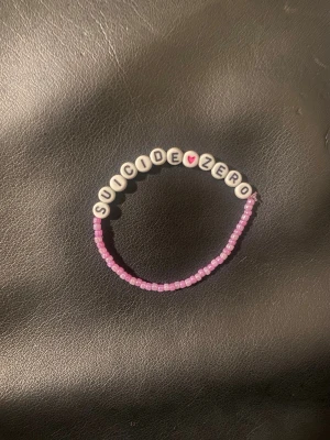 Pärlarmband Suicide Zero rosa - Ett handgjort pärlarmband med texten 'SUICIDE ZERO' i vita bokstavspärlor och ett litet rosa hjärta. Resten av armbandet består av små rosa pärlor. Perfekt accessoar för dig som vill bära ett viktigt budskap.