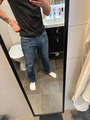 Blå jeans i normal passform - Säljer ett par klassiska blå jeans med normal passform. Jeansen har fem fickor, raka ben och snygga sömmar. Perfekta till vardags och lätta att matcha med olika stilar. Inget synligt märke på bilderna. Storlek 29/30