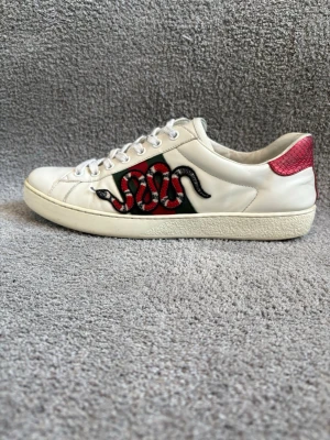 Gucci Ace Snakes - Säljer ett par vita Gucci Ace sneakers i läder med den  broderade ormen på sidan av skon. Skorna är i bra skick, 7,5/10 och mitt pris ligger på 1799kr. Skorna är i storlek 9 vilket motsvarar 43 men passar även 42/44! Dustbag medkommer (se bild 5)  Nypriset för dessa skor är omkring 8000kr. Självklart är skorna Autentiska! Har du några frågor eller funderingar så tveka ej på att skriva!📦🤩