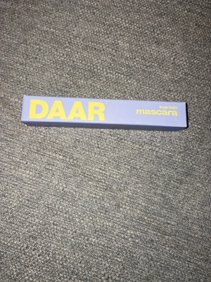 DAAR leap lash mascara lila förpackning - Mascara från DAAR i en stilren lila kartong med stora gula bokstäver. Förpackningen är av kartong och mascaran heter leap lash. Perfekt för dig som vill ha snygga fransar och gillar trendig design.