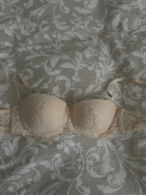 Beige rosa spets-bh med vadderade kupor - Säljer en beige bh med vadderade kupor och vacker spetsdetalj över hela bh:n. Axelbanden är justerbara och ryggen har bred spets. 
