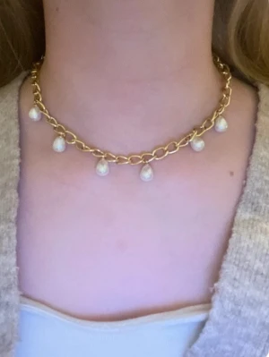 Guldigt halsband med pärldroppar - Rostfritt snyggt halsband i guldtonad plast med större länkar och sju hängande vita pärldroppar. Perfekt för att ge en trendig touch till din outfit. Kedjan har en chunky känsla och pärlorna ger en elegant kontrast.