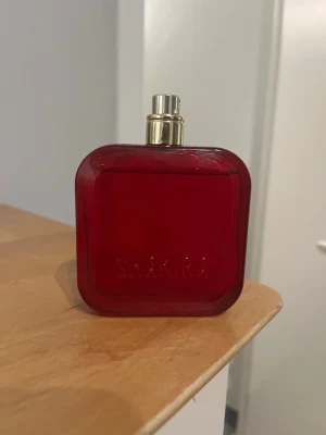 Shakira rojo parfymflaska 80 ml - Snygg parfym från Shakira i en djup röd glasflaska. Flaskan har en modern, fyrkantig form och rymmer 80 ml Eau de Parfum. Perfekt för dig som gillar eleganta och färgstarka dofter. Kork saknas därav billigt pris. Endast använd ett par gånger