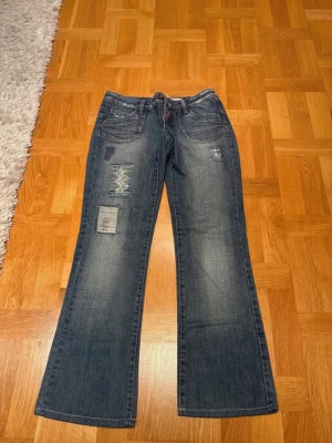 Blå bootcut jeans med slitningar - Säljer ett par blå bootcut jeans med slitningar och patchdetaljer på framsidan. Riktigt snygga men passar tyvärr inte mig. Mått: Midja (tvärs över): 37cm, Innerben: 75cm, Benöppning: 22cm, Gren:19cm. Pris kan diskuteras, hör av dig om du har frågor💕
