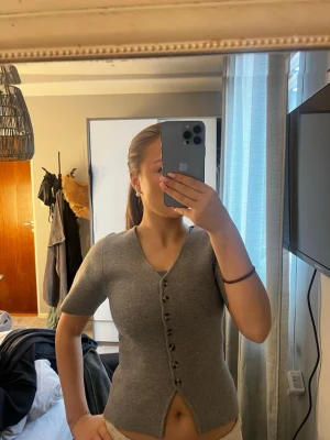 Grå kortärmad kofta med knappar - Säljer en grå kofta med korta ärmar och knappar hela vägen framtill. Koftan har en djup v-ringning. 