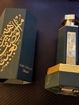 Arabs Collection Obaiah parfym - Lyxig parfymflaska från Arabs Collection, modell Obaiah. Flaskan är mörkgrön med gulddetaljer och har orientaliska mönster i guld på både flaska och förpackning. Designen är elegant och exklusiv, perfekt för dig som gillar unika dofter och snygga flaskor.
