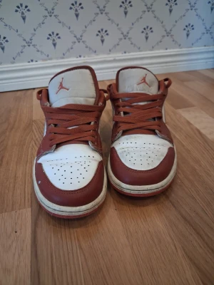 Nike Air Jordan 1 Low röd/vit - Säljer ett par Nike Air Jordan 1 Low sneakers i rött och vitt läder. Klassisk siluett med perforerad tåbox, röda snören som kan behövas bytas då dom är lite dåliga vid toppen och Jumpman-logga på plösen. Swoosh på sidan och kontrasterande vit mellansula. Perfekta för dig som gillar streetwear och ikoniska sneakers. 