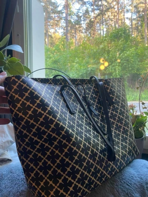 Svart och beige shoppingväska med mönster - Stor shoppingväska i svart och beige med ett grafiskt rutmönster. Väskan har två långa svarta handtag och är tillverkad i ett tåligt material som liknar konstläder. Perfekt för dig som vill ha plats för mycket och gillar en stilren men ändå iögonfallande look.