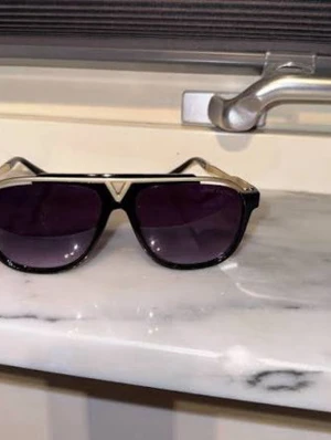 LV glasögon med box! - Snygga svarta solglasögon med markerad guldfärgad metallbåge och mörka glas. Rektangulär form med en cool V-detalj framtill. Perfekta för att höja din stil till nästa nivå.