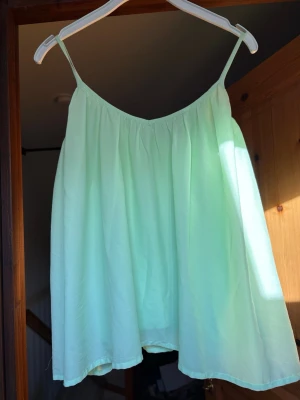 Ljusgrön ärmlös linnetopp - Säljer en ljusgrön, luftig linnetopp med tunna axelband och avslappnad passform. Perfekt för varma dagar och enkel att styla med jeans eller kjol. Toppen har en enkel design utan mönster eller extra detaljer.