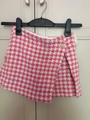 Rutig rosa och vit kjol från Zara - Supersöt kortkjol från H&M i rosa och vitt rutigt mönster. Kjolen har en omlott-look med knappdetalj framtill och är gjord i ett tjockare tyg som ger en lyxig känsla. Perfekt för dig som vill sticka ut med en trendig och färgglad stil.