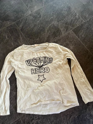 Vit långärmad topp med tryck - Vit långärmad topp med texten 'UPCOMING HERO' och en stjärna framtill. Rund halsringning och avslappnad passform. Perfekt för en chill och avslappnad stil. (Plus frakt) 