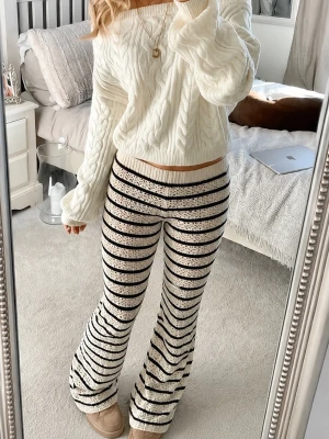 Stickade randiga bootcut byxor med prislappen kvar - HELT OANVÄNDA MED PRISLAPPEN KVAR! Säljer ett par vita stickade loungewear-byxor med svarta horisontella ränder och spetsliknande mönster. Byxorna har utsvängda ben och resår i midjan för extra komfort. Perfekta för sommaren! Helt slutsålda! Storlek S.