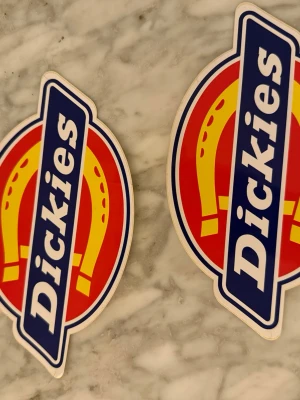 Dickies klistermärken i färg - Två färgglada Dickies klistermärken med klassisk logga i rött, gult, blått och vitt. Perfekta att sätta på datorn, mobilen eller skateboarden för att ge din stil en streetwear-touch.