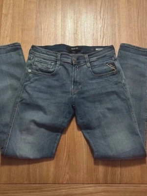 Blå jeans från Replay - Snygga blå jeans från Replay med klassisk femficksdesign och raka ben. Jeansen har en diskret tvättad look och detaljerade sömmar på bakfickorna. Perfekta för en avslappnad och trendig stil. Modell anbass, storlek 28/32, mycket fint skick 