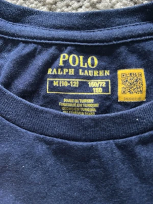 Mörkblå Polo Ralph Lauren t-shirt - Mörkblå t-shirt från Polo Ralph Lauren med klassisk rund hals och tryck av den ikoniska Polo Bear på framsidan. T-shirten har korta ärmar och är tillverkad i mjuk bomull, perfekt för en avslappnad och stilren look.