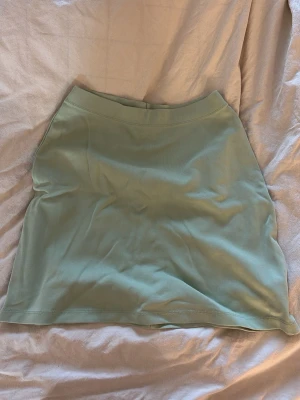 Ljusgrön kortkjol från NLY Trend - Säljer en stilren ljusgrön kortkjol från NLY Trend. Kjolen har en enkel och clean design med rak passform och är tillverkad i ett mjukt material som känns skönt mot huden. Perfekt att matcha med en crop top eller hoodie.