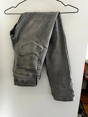 Grå slim jeans j&j - Säljer ett par grå jeans från Jack Jones  med slim passform och klassisk femficksdesign. Jeansen har en snygg tvättad look och är tillverkade i mjukt denimtyg. Perfekta för en avslappnad och stilren outfit.