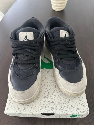 Nike air Jordan 4 rm black and light bone - Snygga Air Jordan sneakers i svart och grått med klassisk Jumpman-logga på plösen. Ovandelen är i en mix av mocka och läder, med svarta skosnören och en robust sula. Perfekta för dig som gillar streetwear och vill ha en ikonisk look.