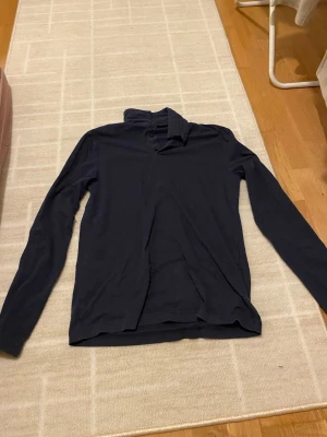 Mörkblå långärmad henley - Mörkblå långärmad henley med klassisk krage och knappar vid halsen. Skjortan har en enkel och stilren design, perfekt för en avslappnad look. Tillverkad i mjukt material som känns skönt mot huden.