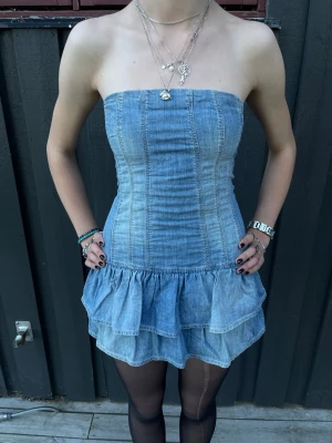 Bandu jeansklänning med volanger - Supercool axelbandslös kort jeansklänning med dubbla volanglager nedtill. Storlek S men den har resår i ryggen så kan kanske passa M med stretchen. Använd en gång så i mycket fint skick☺️💞Den har en underkjol så man slipper oroa sig i vinden (sista bilden)