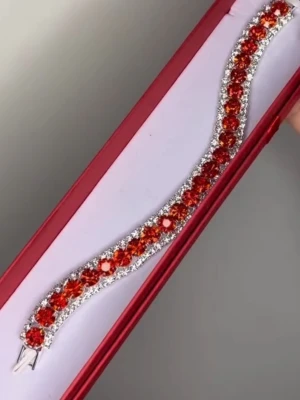 Glittrigt armband med färgade stenar - Snyggt armband med stora, gnistrande stenar i olika färger som rött, blått, guld, rosa och silver. Armbandet har en rad med färgade pärlor omgivna av mindre klara stenar och metall i silverfärg. 