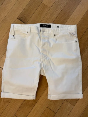 Vita jeansshorts från Replay - Snygga vita jeansshorts från Replay med klassisk femficksdesign. Shortsen har normal passform och är tillverkade i bomull, perfekta för en fräsch och stilren sommarlook. Använda fåtal gånger, väldigt bra skick