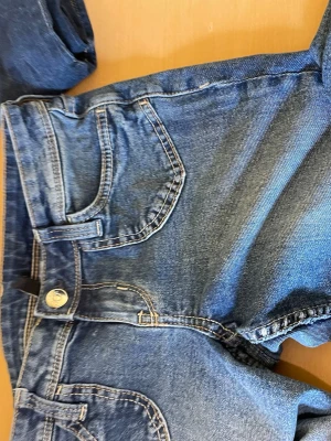 Blå klassiska jeans bootcut  - Snygga blå jeansshorts i klassisk denim med fem fickor och knappstängning. Shortsen har en normal passform och är perfekta för varma dagar. Tillverkade i bomull för en skön känsla och slitstark look. De är super low waist och jättebra material. Jag är 152 behövde klippa nere men den är ftf ganska lång på mig. Med klackar är de super snygg så passa på!!