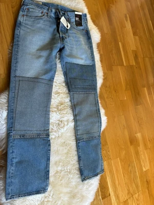 Levi's 501 patchwork jeans blå - Säljer ett par Levi's 501 Original jeans i ljusblå denim med coola patchwork-detaljer på benen. Klassisk rak passform, fem fickor och knappgylf. Perfekta för dig som vill sticka ut med en unik stil. Material: 100% bomull.
