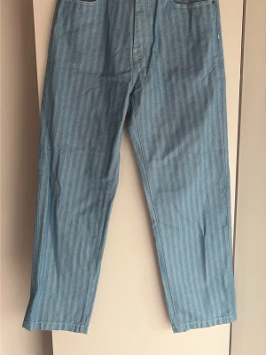 Randiga ljusblå jeans från Carhartt - Säljer ett par ljusblå jeans från Carhartt med vertikala ränder. Klassisk femficksmodell med raka ben och hög midja. Jeansen är tillverkade i slitstark denim och har en patch med Carhartt-loggan bak på ena fickan.