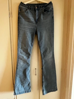 Blå bootcut jeans med hög midja - Snygga blå bootcut jeans med klassisk femficksdesign och hög midja. Jeansen har en lätt tvättad look och raka ben som går ut lite nertill. Perfekta för en avslappnad och trendig stil. Materialet är denim i bomull.