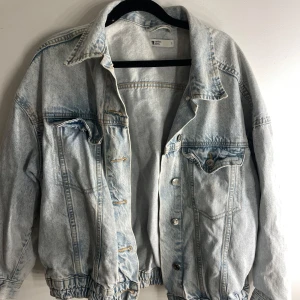 Ljusblå jeansjacka från Gina Tricot - Säljer en ljusblå jeansjacka från Gina Tricot. Jackan har en klassisk design med knappar framtill och två bröstfickor. Den har en lite oversize passform och elastisk nederkant för extra detalj. En fläk på ena axeln ca💕
