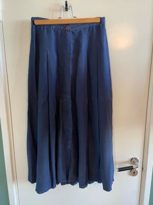 Blå långkjol i äkta siden - vintage - Snygg blå långkjol med knäppning fram och fina veck. A-linje, smal midja och vid längst ner. Vackert fall i tyget på grund av det fina materialet. Italiensk vintage, liten italiensk storlek – det står 44 på lappen men motsvarar ungefär 36–38. 