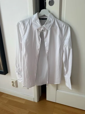 Vit klassisk skjorta från Zara - Klassisk vit skjorta från Zara med lång ärm och knappar framtill. Skjortan har en tidlös krage och är gjord i ett mjukt bomullstyg som känns skönt mot huden. Perfekt basplagg till garderoben och enkel att styla. Obs, liten storlek.