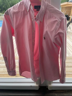 Rosa skjorta från Ralph Lauren - Klassisk rosa skjorta från Ralph Lauren med button-down krage och broderad logga på bröstet. Skjortan har långa ärmar och knappar framtill. Tillverkad i mjuk bomull som känns skön mot huden. Perfekt för en stilren och avslappnad look. Ny pris 1750 säljer för 1100 pris kan diskuteras den är helt ny och aldrig använts den va för liten darför säljer jag