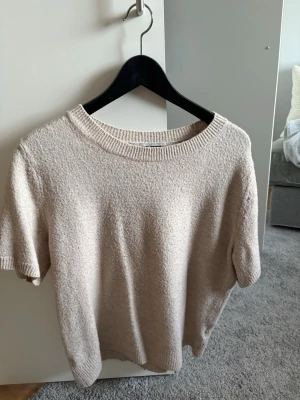 Beige kortärmad stickad tröja - Mysig beige stickad tröja med korta ärmar och rund ringning. 
