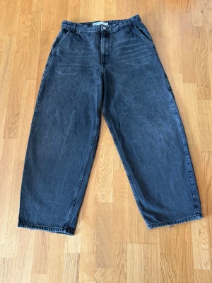 Baggy svarta jeans - Säljer ett par svarta baggy jeans med raka ben och hög midja. Jeansen har klassiska fem fickor och stängs med knapp och dragkedja. Perfekta för en avslappnad streetstil och tillverkade i kraftig denim.