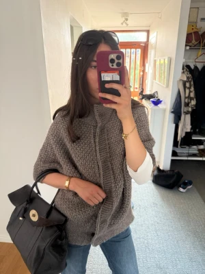 Brun stickad poncho med dragkedja - Säljer en brun skickad supersöt kofta med knappar framtill med hög krage.  Perfekt att slänga över en långärmad tröja. Passar till jeans för en chill och snygg look.